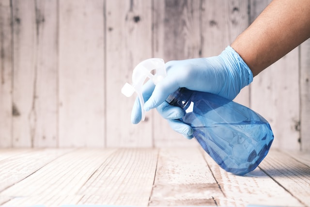 A person using a blue spray bottle with blue gloves to clean wooden floors and panneling, an excellent way to prevent rats prior to rodent season