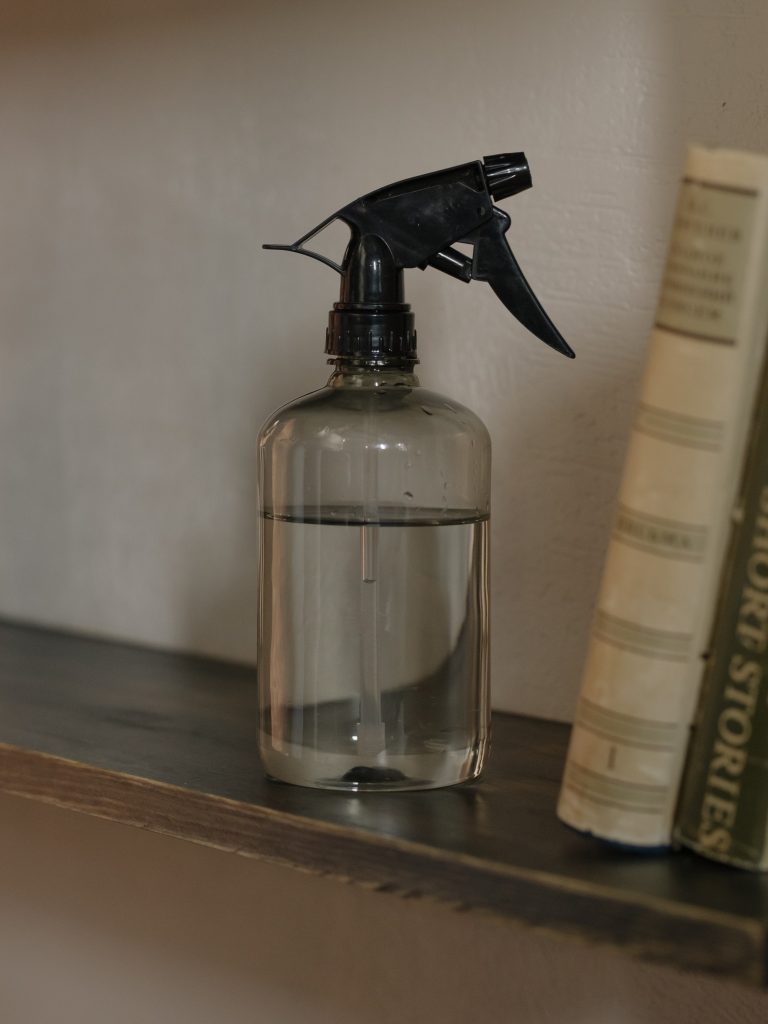 Spray bottle filled with clear liquid next to stack of tan and brown books