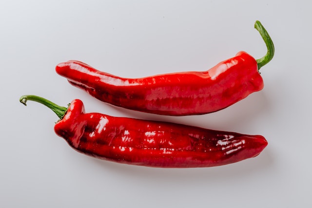 Two red cayenne peppers on a white surface 