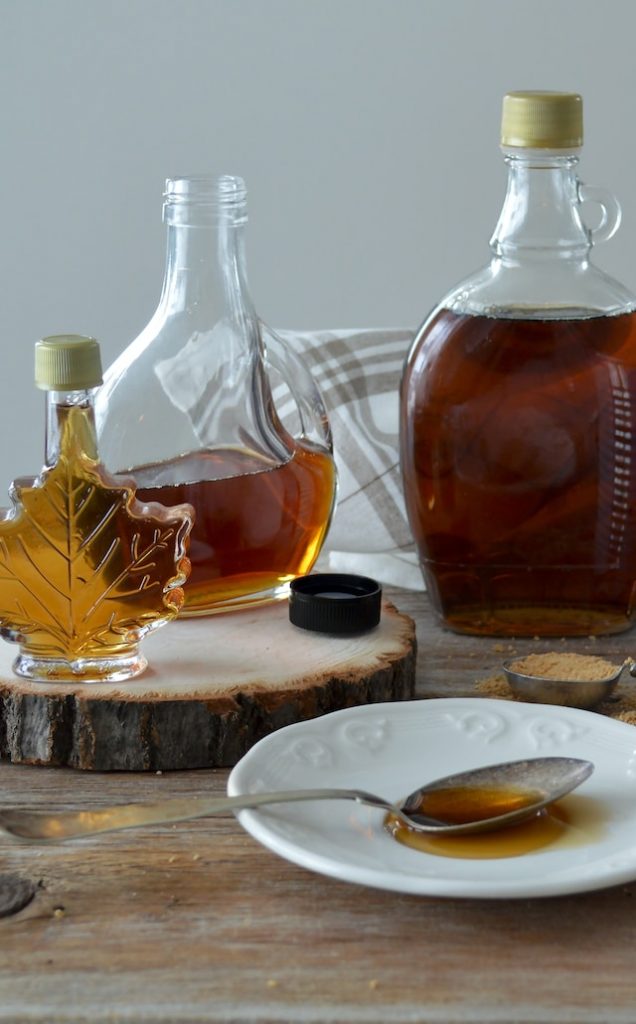 multiple bottles of maple syrup surrounding a white plate