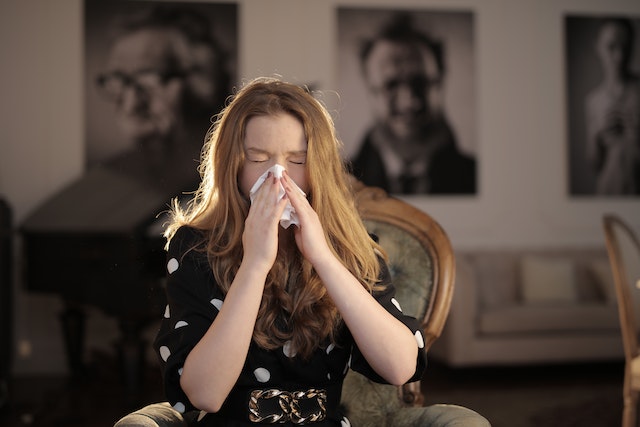 Red-headed woman sneezing into a tissue