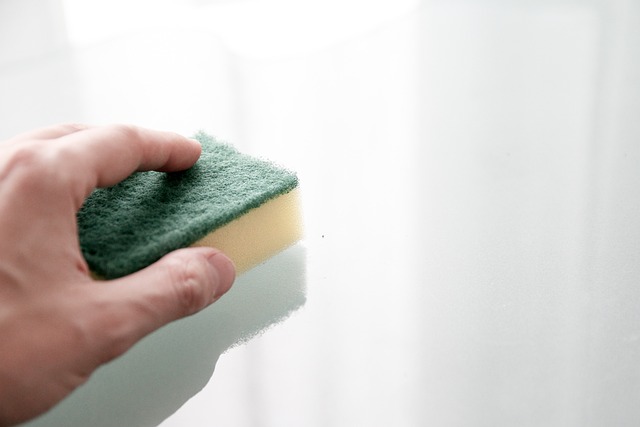 Person cleaning a kitchen countertop with a green and yellow sponge 