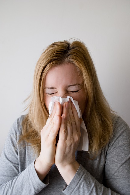 blonde woman sneezing into a white kleenex tissue